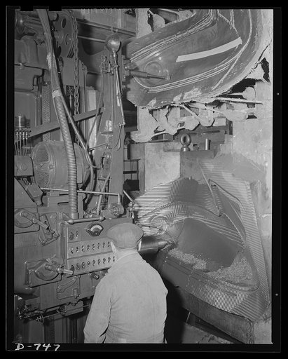 A Keller machine cutting a die shape from a plaster model. The model is at the top. A "feeler" tool runs along the surface of the model and controls the cutting tool at the bottom in such a manner that the contours of the model are duplicated with an extremely high degree of precision in the cast-ir