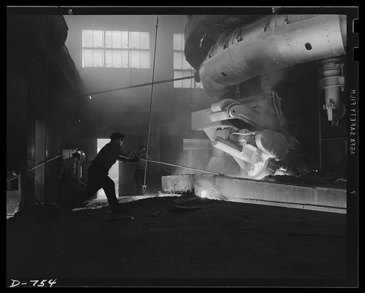 After a casting is completed, a compressed air gun plugs the furnace wall with nine cubic feet of clay. Workers wear asbestos suits to shield them from the heat. Ford River Rouge plant, May 1941