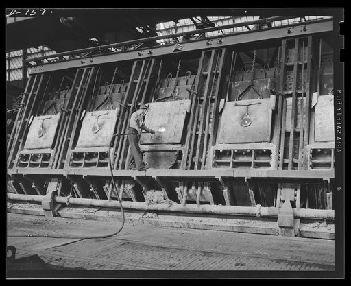Molten metal from blast furnaces arrives at the open hearth foundry where it is placed in a 600 ton mixing furnace, which maintains a temperature of 2100 degrees fahrenheit. The mixing furnace acts as a sort of thermos bottle, or ore storage tank. A worker is shown here preparing an open hearth furn