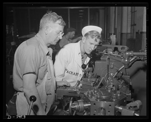 A Navy student observing screw machine operations in the making of a crankshaft bearing cap bolt. Packard marine engine plant, Detroit