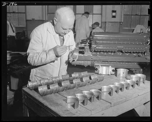 At several stages during their manufacture, the engines are subjected to exacting tests. Here a skilled machinist is inspecting the main and connecting rod bearings of an engine that has been run on the test block, then dismantled to determine the amount of stress and wear it has suffered. Packard m