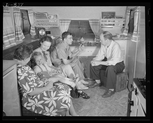 Defense housing, Erie, Pennsylvania. Typical of the many families to take advantage of the defense trailer camp in Erie, Pennsylvania, is B.J. Rogan (right), his wife (third from right), and small son. They are shown here inside their trailer home, chatting with neighbors. Rogan is employed as a dri
