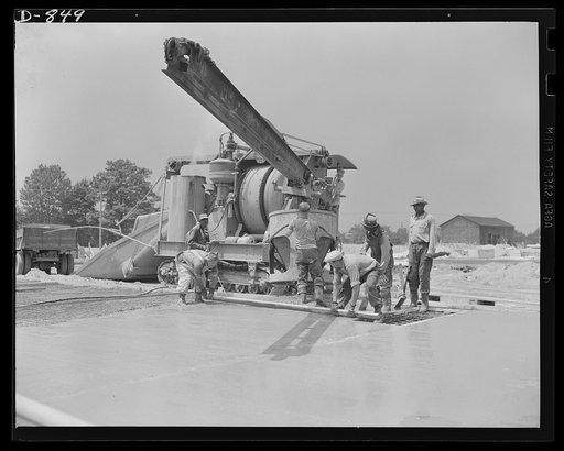 Defense housing, Erie, Pennsylvania. Concrete flooring is poured over wire reinforcements. The large container shuttles from the mixer to the desired location, supported by a movable crane. Three men, aided by a crew of levelers, can lay a floor of a four-unit building in a few hours