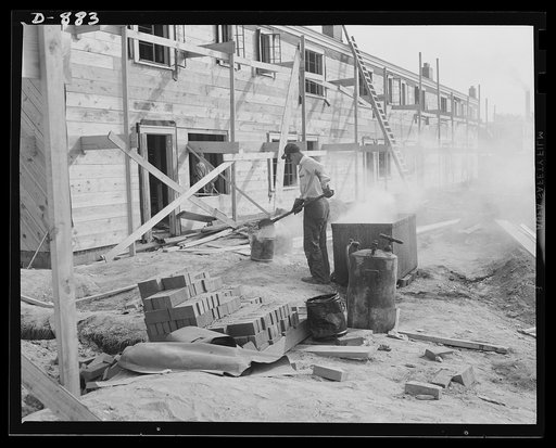 Defense housing, Erie, Pennsylvania. A built-up roofing is applied to the individual unit. Here a workman tends to the vat in which the pitch is kept molten. Pitch is hoisted to the roof in buckets