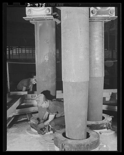 Steel alloy manufacture. Allegheny Ludlum Steel Corporation, Brackenridge, Pennsylvania. The huge carbon electrodes of the thirty-five ton electric melting furnaces used in converting scrap iron and steel into high quality alloy steels. A worker is adjusting the rings that guide the electrodes into 