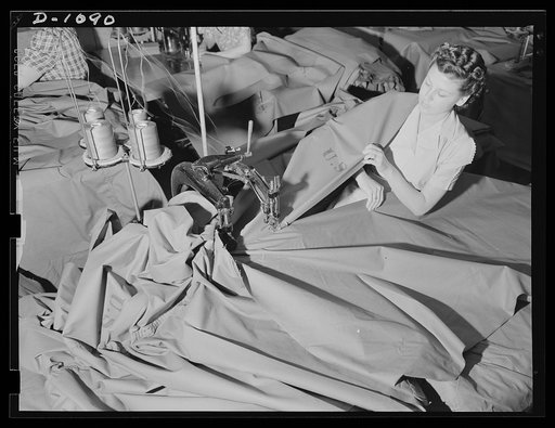Langdon Tent and Awning Company, Wichita, Kansas. With the grade and dexterity of master dressmaker this attractive young woman fabricates "pup" tents for the expanding defense Army. A two-needle felling machine joins two widths of cloth to form the main body of the tent