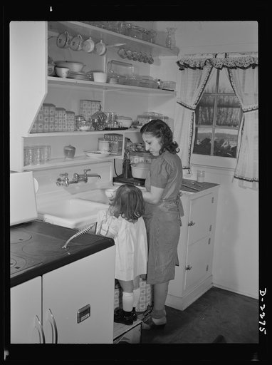 Bantam, Connecticut. Defense homes. Little Ann Heath is eager to try out all the facilities of her parents' new four-room defense housing unit, after spending most of her life in a single furnished room. Here she pushes her footstool to the sink in order to help her mother clean up the dinner dishes