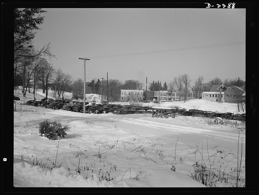 Bantam, Connecticut. In the background is the Warren McArthur plant. The cars in the foreground belong to workers in the plant, at least half of whom commute from nearby towns and cities. Between the cars and the bridge runs a track along which, once daily, a train pulls up with feed and grain for B