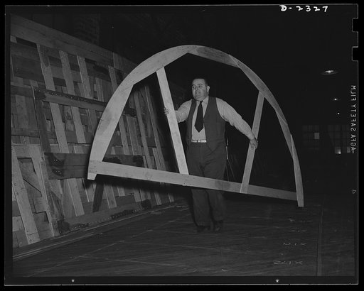 Shipbuilding. "Liberty" ships. Wooden templates are used as patterns for the laying out of a number of steel plates. This worker is carrying the template for a gun foundation from the mold loft to the plate working section. All parts are prefabricated in this huge Eastern plant which formerly turned