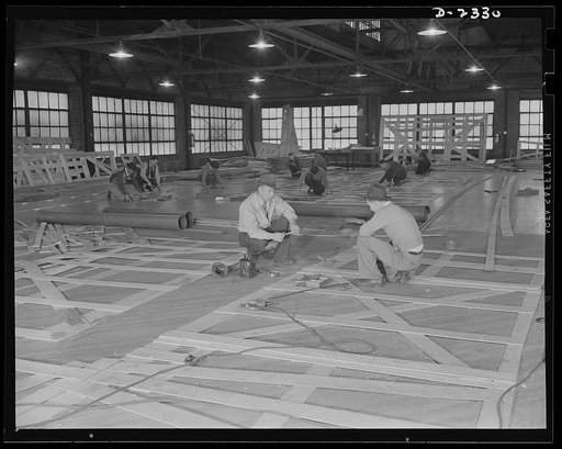 Shipbuilding. "Liberty" ships. Wooden templates are used as patterns for the laying out of a number of steel plates. These workers are transferring the templates designs, or patterns, to steel, to be used in ships under construction at a large Eastern shipyard. All parts are prefabricated in this hu