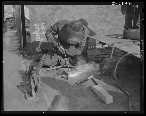 Shipbuilding. "Liberty" ships. Ratchets, turnbuckles and "dogs" hold these deck units of a new Liberty ship in place as a welder in a large Eastern shipyard uses the torch to fuse them