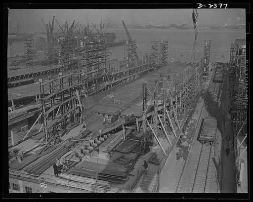 Shipbuilding. "Liberty" ships. A new vessel has just moved off these ways, and the keel is being assembled for yet another, in a large Eastern yard. The bottom and side shell plating and the inner tank sections are being assembled. Another new keel has been laid on the ways to the left. All parts ar