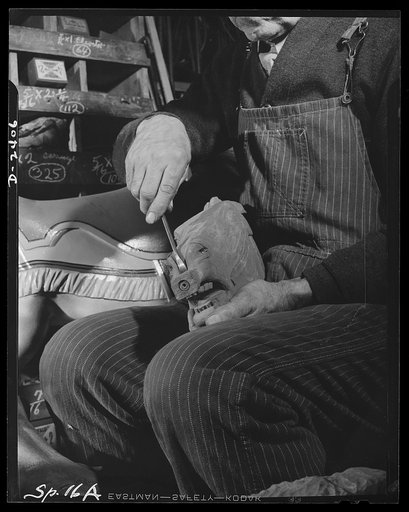 Conversion. Merry-go-round plant. These skilled hands belong to sixty-five-year-old Herman Jagow, whose wood carving skill delighted thousands of children riding the horses of merry-go-rounds. Here he is finishing up some carvings. Jagow spends most of his time now in lathe work for the war program.