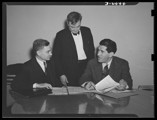 Thomas C. Blaisdell, Assistant Director of the National Resources Planning Board (left); Robert R. Nathan, Assistant Director of Progress Reports, War Production Board (right); and Fred Searles, Consultant on Ordnance, Ammunition Division, U.S. Army(standing). The three-man planning committee which 