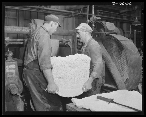 Synthetic rubber (Ameripol). These workers are removing crumbs from the perforated boxes below the coagulating and extractor tanks. The rubber drips into these boxes from the tanks and the water previously added to dissolve the soap in the solution runs off through the perforations in the box. This 