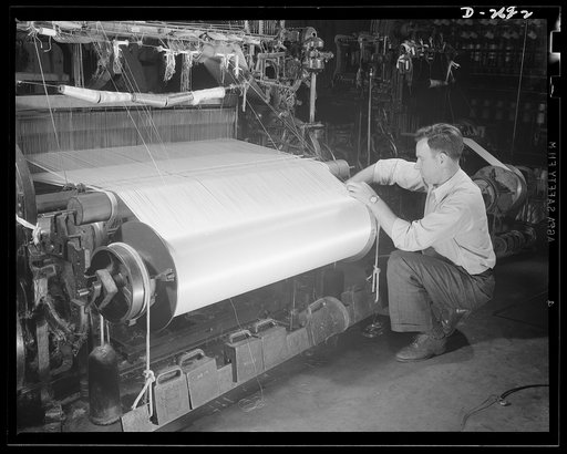 Fiberglass manufacture, Owens-Corning, Toledo, Ohio. A warp beam of fine fiberglass yarns being put into a loom preparatory to weaving all-glass fabrics used to make electrical insulation, pipe lagging for naval vessels, and industrial service fabrics where high tensile strength, resistance to corro