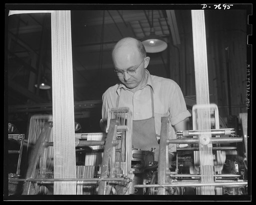 Fiberglass manufacture, Owens-Corning, Toledo, Ohio. From an overhead feed, two bands of all-glass warp yarns are fed into a standard type loom that converts them into a narrow fiberglass fabric to wrap high-pressure steam lines on modern war vessels