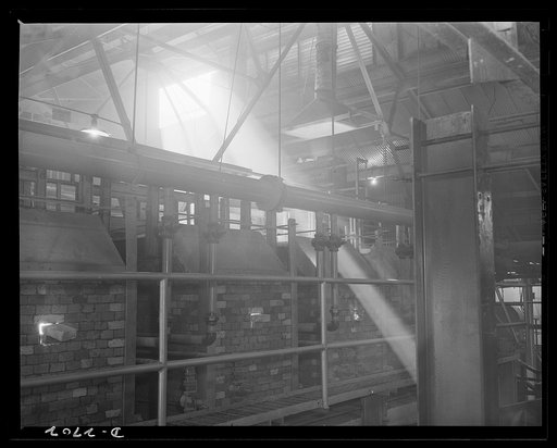 Fiberglass manufacture, Owens-Corning, Toledo, Ohio. Glass-making goes around the clock. A shaft of twilight sun illuminates a huge glass furnace that is converting a carefully compounded batch into molten glass than will be drawn into fine, resilient fibers. The fiberglass insulating wool produced 