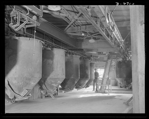 Fiberglass manufacture, Owens-Corning, Toledo, Ohio. Along an overhead monorail system, cans containing the carefully compounded ingredients of the batch move to the huge furnaces for conversion into molten glass from which fiberglass materials are manufactured in a plant of Owens-Corning Fiberglass