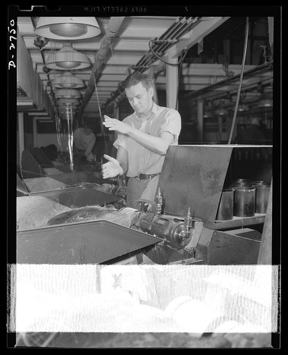 Fiberglass manufacture, Owens-Corning, Toledo, Ohio. A worker in a plant of the Owens-Corning Fiberglass Corporation guides a strand of 204 glass filaments from the forming machine above to the gathering tube on which it is wound at more than a mile a minute