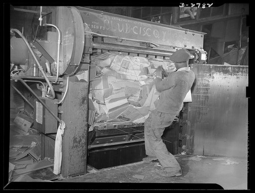 Scrap collection. The door of the baling press is opened. This picture shows how the bottom of the press has moved up and compressed the cardboard into a small bundle. Wires are passed around the bundle, and the man here is pulling the wire tight with pliers. Shapiro Company, Baltimore, Maryland
