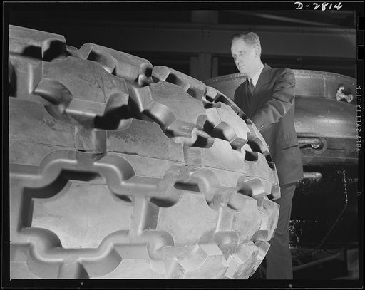 Giant tire manufacturer. Final inspection of the world's largest tire, the 36.00-40 earth mover, used in the construction of airports and new army camps. This huge tire stands nine and a half feet high, with tube and flap, weighs 3,646 pounds and carries 55,000 pounds. The giant mold in which it is 
