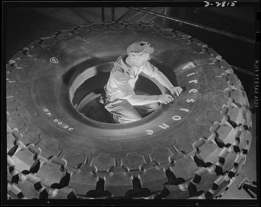 Giant tire manufacturer. Final inspection of the world's largest tire, the 36.00-40 earth mover, used in the construction of airports and new army camps. This huge tire stands nine and a half feet high, with tube and flap, weighs 3,646 pounds and carries 55,000 pounds. The giant mold in which it is 