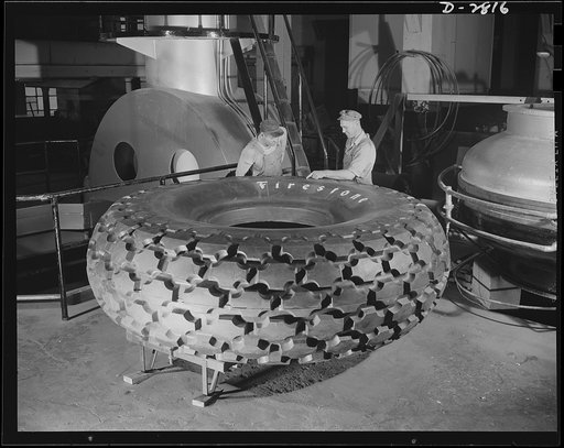 Giant tire manufacturer. Final inspection of the world's largest tire, the 36.00-40 earth mover, used in the construction of airports and new army camps. This huge tire stands nine and a half feet high, with tube and flap, weighs 3,646 pounds and carries 55,000 pounds. The giant mold in which it is 