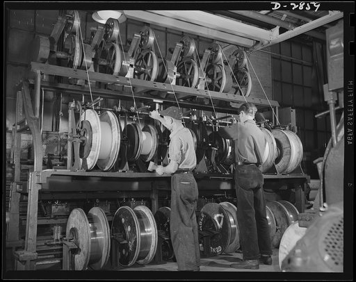 Transformer manufacture. Flowing at the rate of ninety feet per minute, the flattened copper wire is wrapped with insulating tape by these machines. The workers pictured here stand by ready to change spools. Westinghouse, Sharon, Pennsylvania