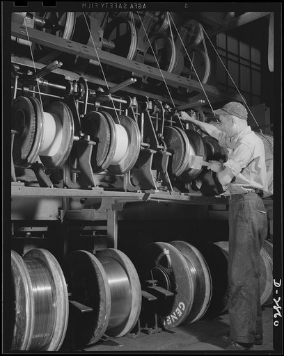 Transformer manufacture. Flowing at the rate of ninety feet per minute, the flattened copper wire is wrapped with insulating tape by these machines. The workers pictured here stand by ready to change spools. Westinghouse, Sharon, Pennsylvania
