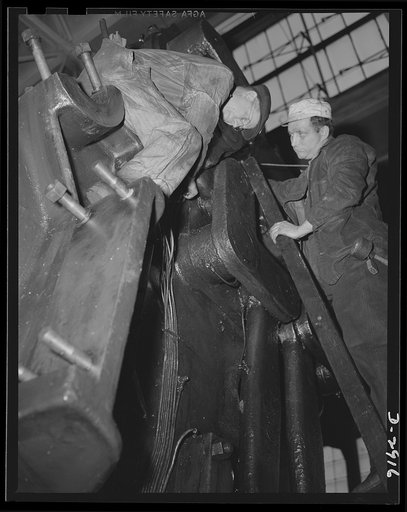 Conversion. Automobile plant. Assembling oil distribution pipes to back shaft, flywheel, and clutch mechanism bearings of a huge 90T96 Cleveland press being relocated to perform a major operation on hood panels for 4 x 4 army trucks. The 120-ton machine was moved piece by piece from another plant th