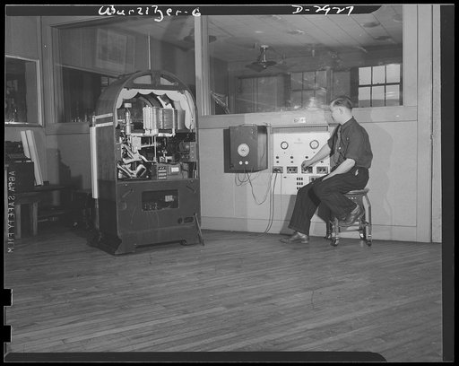 Conversion. Jukebox plant. As indigenous to the American scene as the hamburger stand and Mickey Mouse, juke boxes like this, here being tested. From now on, electrical control instruments, based on the principle of the jukebox selection device, will be produced here for use by Uncle Sam's armed for