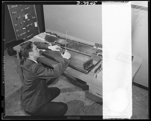 Conversion. Silverware plant. To meet Air Corps Ordnance specifications, this bomb shackle must be accurate to the 1/10,000th of an inch, and that's pretty tight measuring by anybody's standards. An employee of an Eastern plant which produced silver tableware in peacetimes, inspects the shackle aide