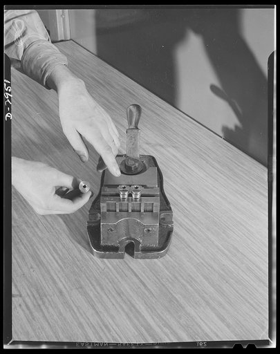 Conversion. Silverware plant. An Eastern factory which produces bomb shackles for Uncle Sam's birdmen was once one of the country's best-known manufacturers of table silver. Above is closeup of a shaft assembly in specially made milling jig. Held at left is unmilled shaft while at right are complete