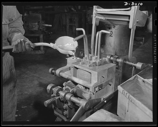 Aluminum casting. Ladling of molten aluminum alloy into the gate of a closed permanent mold. Site of these operations is a large Midwest aluminum foundry now converted to production of essentials for America's armed forces. The part being cast here may be destined for the engine of a "jeep" or part 