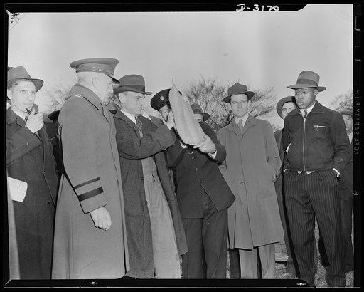 Director J. M. Landis, Office of Civilian Defense (center) shows how the sandbag with hand grip can be used as a face protector in fighting incendiary bomb. Left is Major General L. D. Gasser, head of Protection Division, Office of Civilian Defense. Constable Scott of London (right) holds one end of
