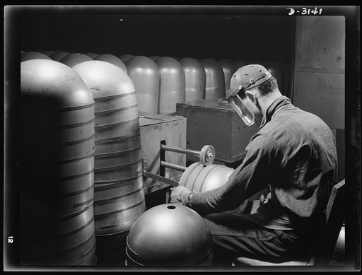 Conversion. Beverage containers to aviation oxygen cylinders. After the circumferential straps are welded to the cylindrical portion, in the metal division of a large Eastern rubber factory, rough edges and accumulated weld scale are removed by a skilled workman. The twin rotary brushes, shown above
