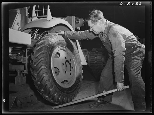 Mounting a wheel on a halftrac scout car is made as simple a job as possible. The soldier in the field won't have the uniform working conditions of the man on an Ohio assembly line, but the tire mounting job is the same. White Motor Company, Cleveland, Ohio