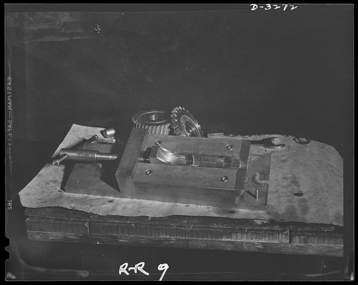 Oil burners to machine gun parts. Fixture which holds bare of raw materials from which small pieces, cut to size, are obtained for production of precision parts for Uncle Sam's machine gun squads. Site of these operations is an Eastern factory which has been converted from manufacture of oil burners