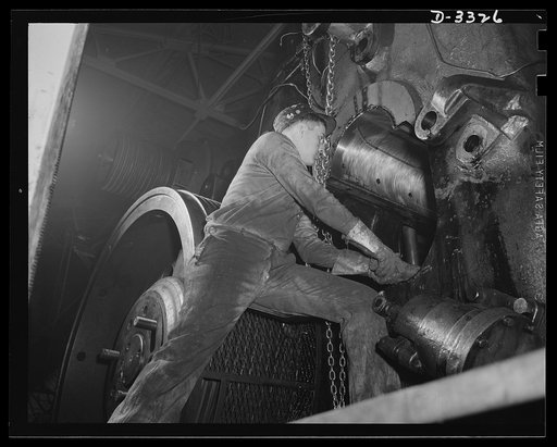 America's automobile industry changes over to war production. A huge forge hammer which formerly made parts for a well-known car is being converted for producing ammunition. Oldsmobile, Lansing, Michigan