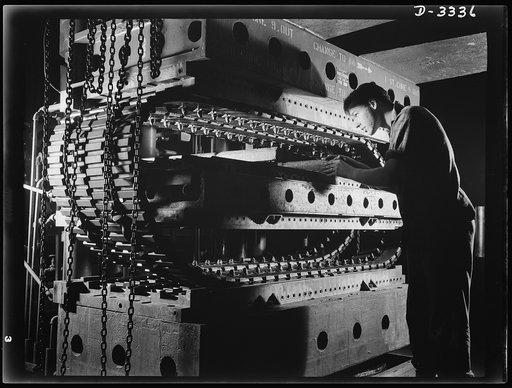 A pair of tracks for an Army halftrac car comes from the hydraulic curing press of a Midwest tire plant in nearly complete form. Wooden slide bars facilitate. Goodrich, Akron, Ohio