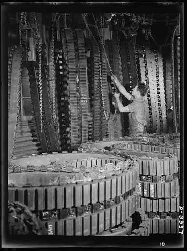 A huge and rapidly increasing supply of tracks for Army halftrac cars comes from one Ohio tire plant alone. Traveling chain hoists carry tracks from the curing press to trimming racks on which curing plates and overflowing edges of rubber are removed. Goodrich, Akron, Ohio