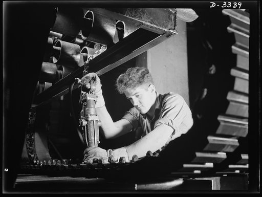 A track for an Army halftrac car nears completion as curing plates nuts are removed with an air pressure wrench on the trimming rack of a Midwest rubber plant. Goodrich, Akron, Ohio