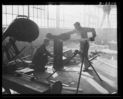 Twenty-millimeter machine guns for planes. The conversion of a big auto manufacturing plant to production of machine guns for the Air Corps continues without letup until the job is done. Electricians extending power lines are often among the first at the new machine locations. Oldsmobile, Lansing, M