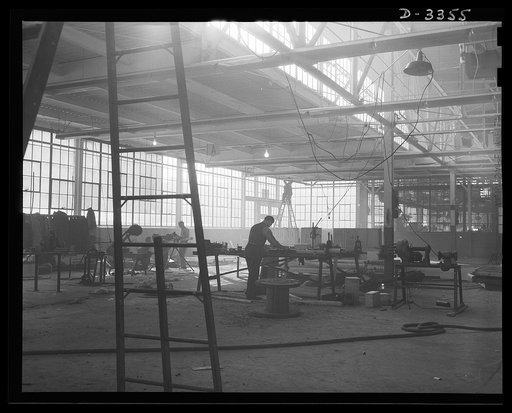 Twenty-millimeter machine guns for planes. Day and night, the conversion of a big auto manufacturing plant to the production of machine guns for the Air Corps continues without letup until the job is done. Electricians extending power lines are often among the first at the new machine locations. Old