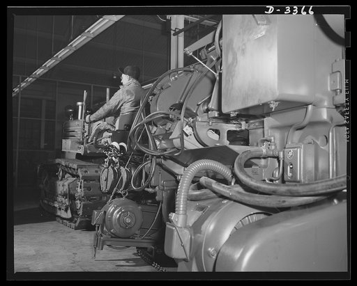 Twenty-millimeter machine guns for planes. Another machine is skidded into place in a converted auto plant to swell the production of machine guns for the Air Corps. Oldsmobile, Lansing, Michigan