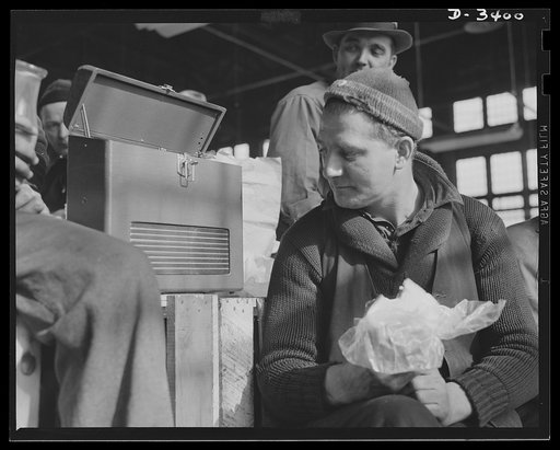 Conversion. Heaters to bogie wheels. How'd it go today with the boys at Bataan? These employees of a Midwest heater company take time out for lunch and the news before resuming work on installing assembly apparatus for M-4 tank bogie wheels in a company warehouse