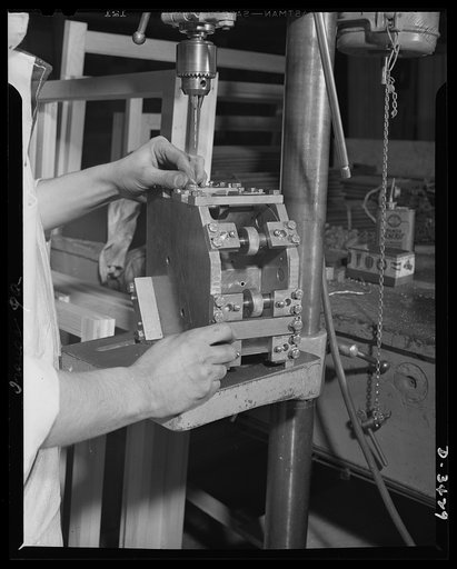 Conversion. Metal screens to bomber windows. An aluminum switch box for an airplane tow target is drilled in a production jig at an Eastern plant that formerly made metal screens for doors and windows