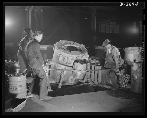 One of the many intricate performances necessary to the production of aluminum parts for Uncle Sam's mechanized army involves the tapping of a pound tilting type crucible furnace to obtain flow of molten metal into the smaller pot. Aluminum Industries