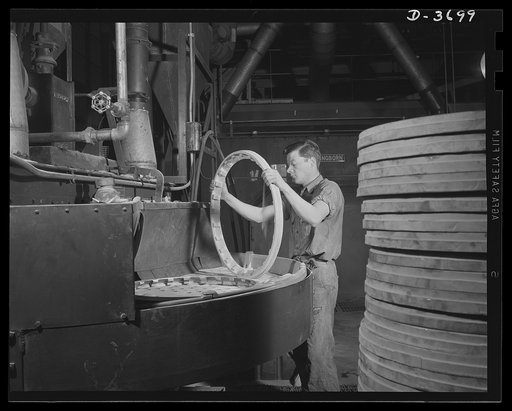 Loading castings onto a sandblast table in a large Midwest aluminum foundry now producing war essentials